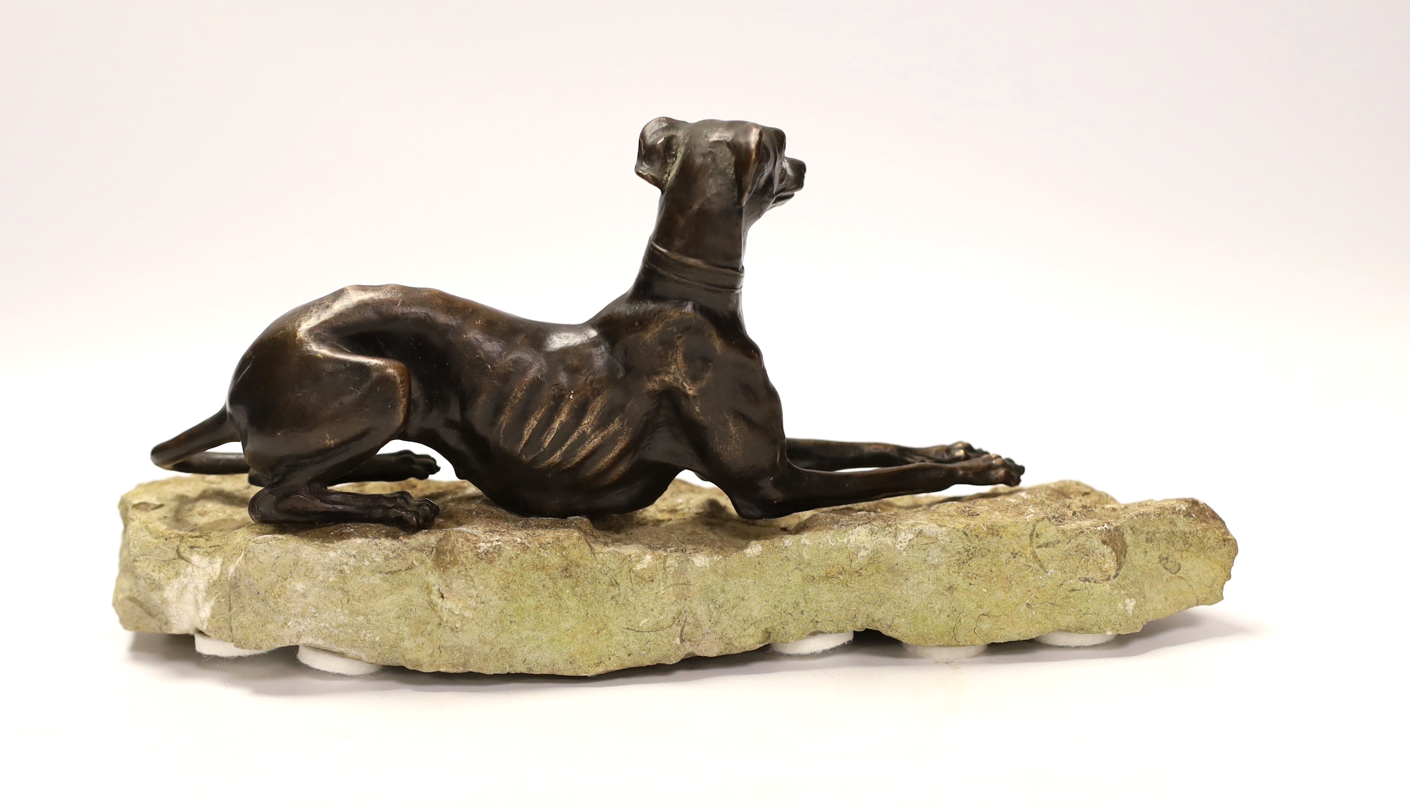 A bronze model of a recumbent greyhound on a rough-hewn limestone base, 27cm long